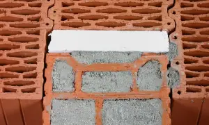 Zbliżenie na fragment ściany z pustaków ceramicznych, zaprawy i białego elementu izolacyjnego.