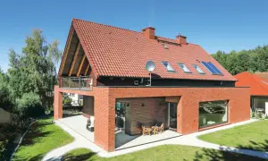 Nowoczesny dom z czerwonej cegły i dachem dwuspadowym, z balkonem i oknami dachowymi.
