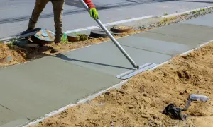 Robotnik wygładza świeży beton na budowie chodnika za pomocą kielni.