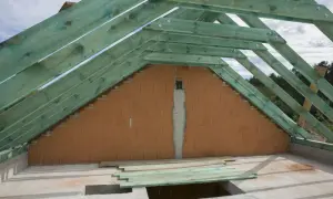 Konstrukcja dachu z zielonych krokwi i ściany szczytowej z cegły.