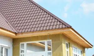 Drewniane deski tworzą wykończenie okapu dachu, nad którym widać brązową dachówkę. Budynek jest ocieplony żółtą wełną mineralną.