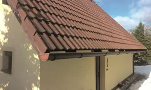 Brązowy rynna dachowa pod czerwonym, dachówkowym dachem domu.