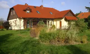 Dom z czerwonym dachem i naczółkami, otoczony zielonym trawnikiem i ozdobnymi trawami.