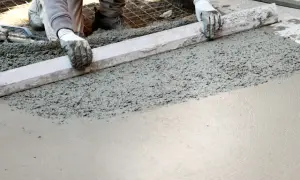 Ręce w rękawiczkach wyrównują świeży beton za pomocą łaty.