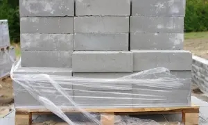 Stos szarych bloczków betonowych na palecie, owiniętych folią. Poznaj bloczek betonowy wymiary i zacznij budowę!