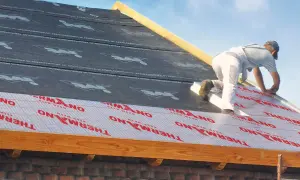 Pracownik montuje izolację nakrokwiową na dachu.