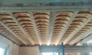 Widok od dołu na strop w domu parterowym, z widocznymi belkami stropowymi i pustakami ceramicznymi.