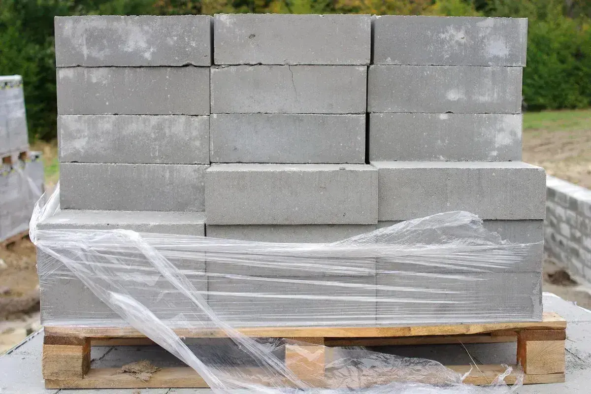 Stos szarych bloczków betonowych na palecie, owiniętych folią. Poznaj bloczek betonowy wymiary i zacznij budowę!