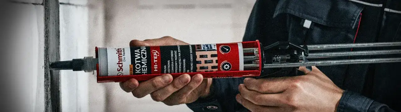 Dłoń trzyma pistolet z kartuszem kotwy chemicznej, gotowa do użycia kotwy murarskie do mocowania elementów.