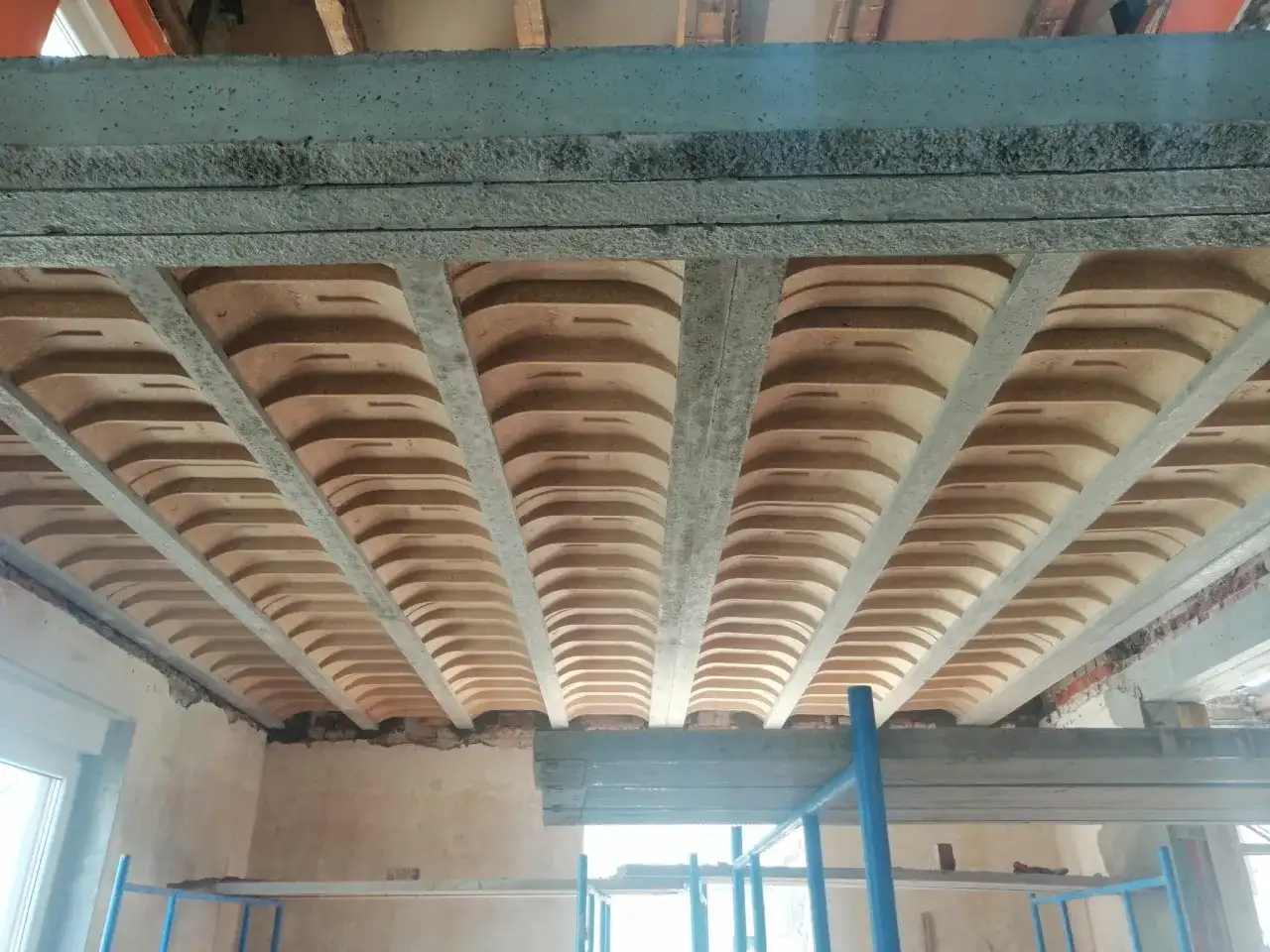 Widok od dołu na strop w domu parterowym, z widocznymi belkami stropowymi i pustakami ceramicznymi.