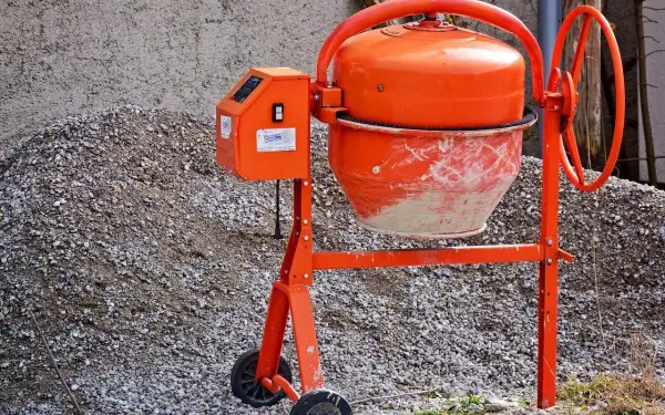 Pomarańczowa betoniarka czeka na materiały, by pokazać, jak zrobić beton. Obok stos kruszywa.