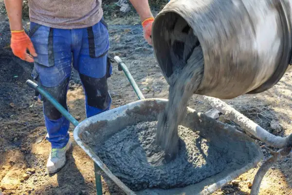 Betoniarka wylewa beton do taczki, pracownik w rękawicach stoi obok.