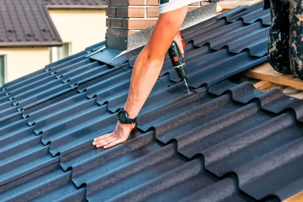 Dachówka ceramiczna, pracownik dokręca wkręt w dachu w pobliżu komina.