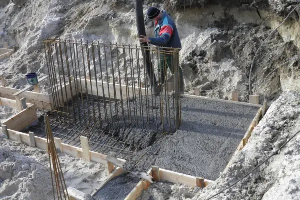 Budowa fundamentów: pracownik wylewa beton do szalunku zbrojonego.