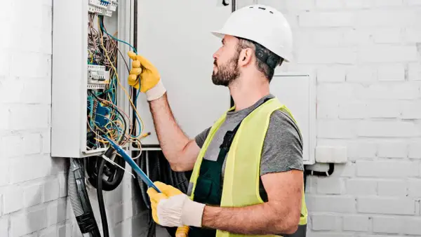 Elektryk w kasku i kamizelce odblaskowej pracuje przy skrzynce z przewodami.