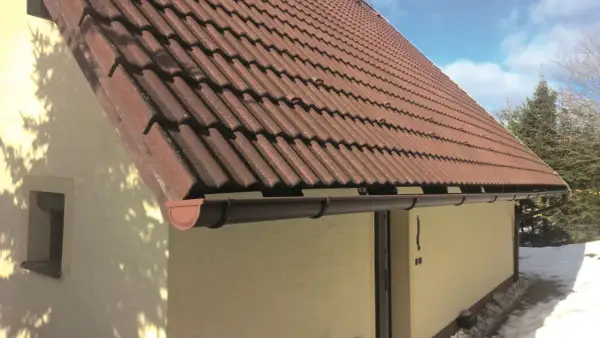 Brązowy rynna dachowa pod czerwonym, dachówkowym dachem domu.