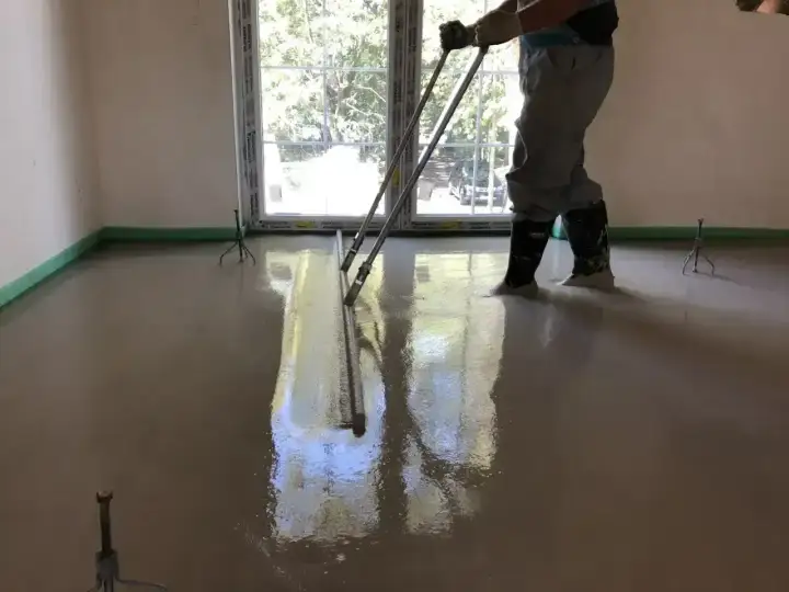 Pracownik wylewa betonową podłogę, sprawdzając, ile materiału potrzeba na m2.
